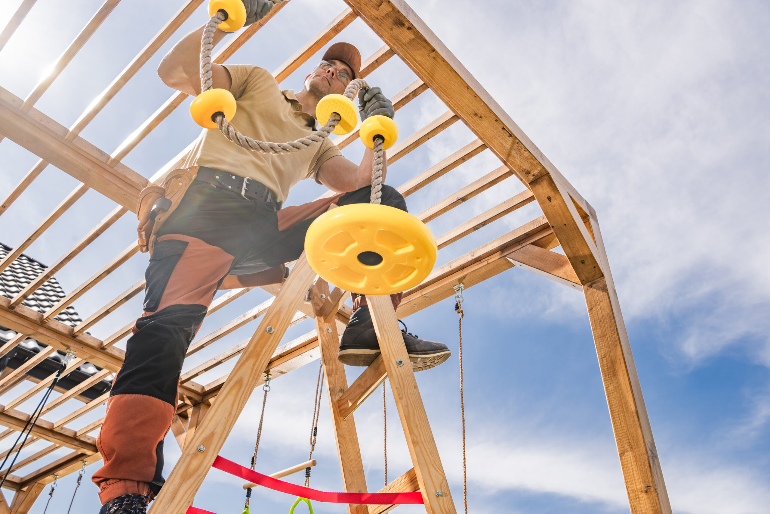 Worker assembling a wooden playset with rope features and climbing structures – Swing Set & Playset Installation