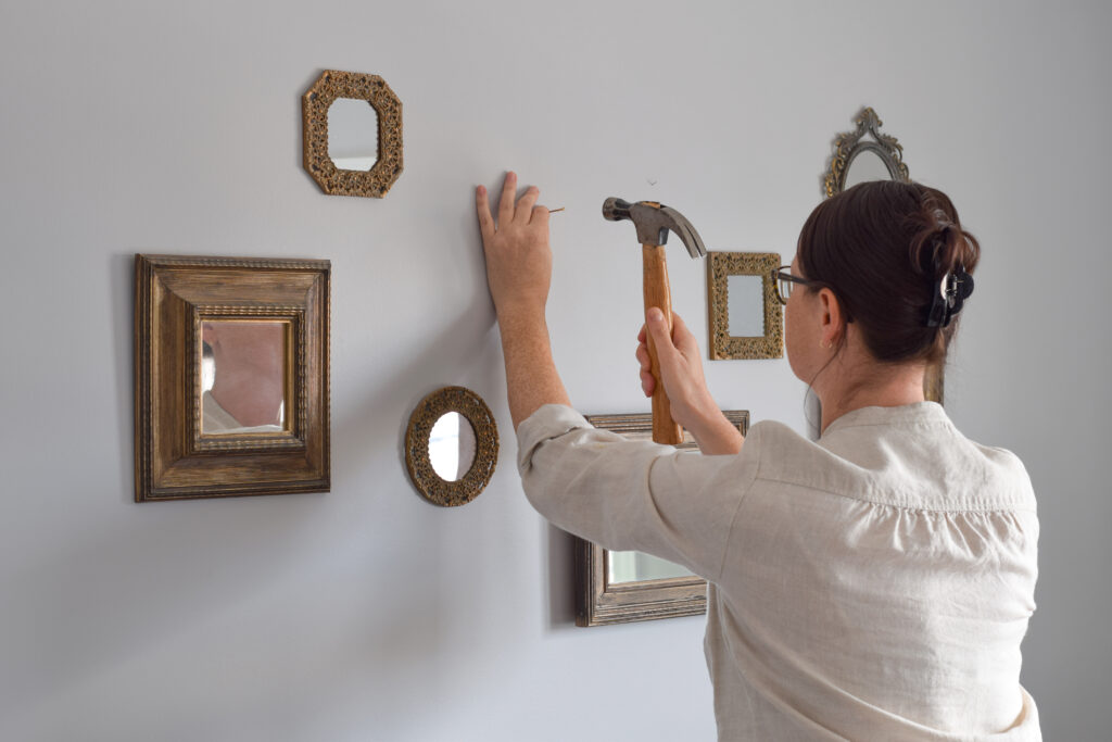 Woman hanging vintage-style mirrors with a hammer, showcasing wall art and mirror installation expertise.